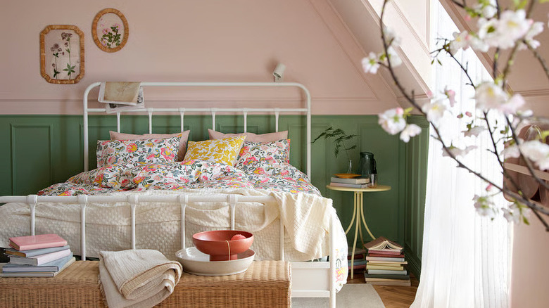 A bed is made with floral sheets in a light-filled pink and green room