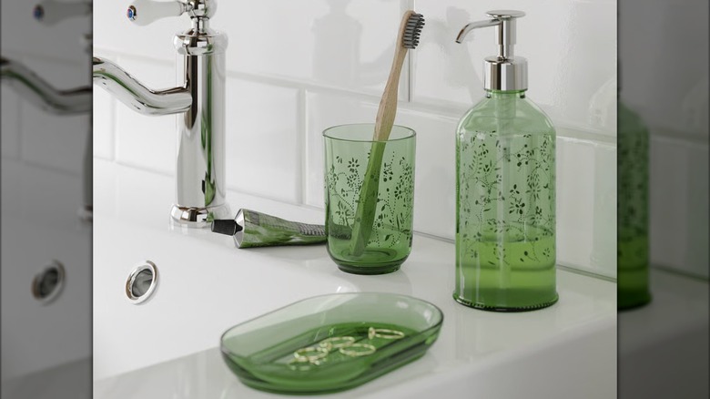 Three green glass bathroom organizers sit on a white sink basin