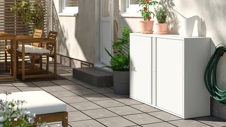 A small tomato plant and watering can sit on a white SUNDSÖ Cabinet from IKEA outside on a patio