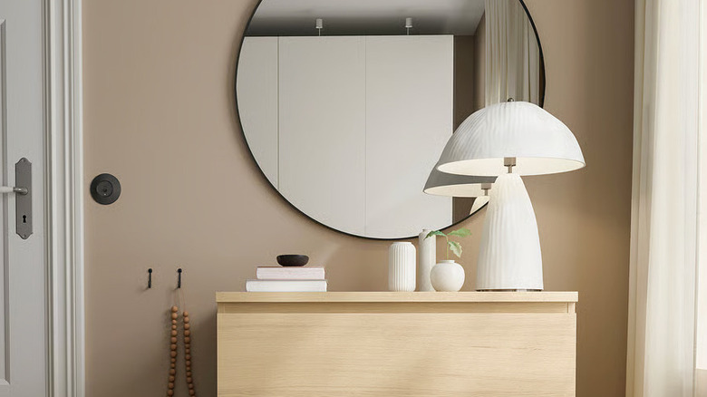 An unusual white lamp sits on a wooden dresser in front of a large round mirror