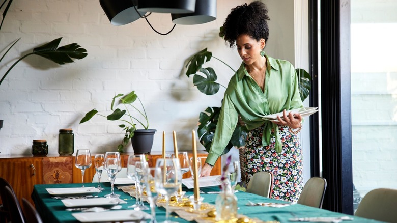 Woman putting place settings at table to prepare for hosting a party