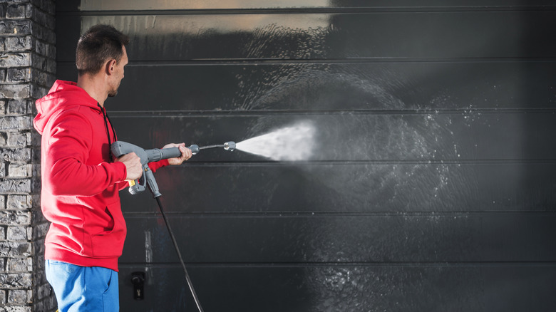 Man in a red sweatshirt using a pressure washer to clean a garage door