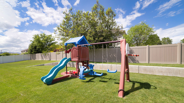 A kids' playset with slide, swings, and sandbox in a backyard on a sunny day