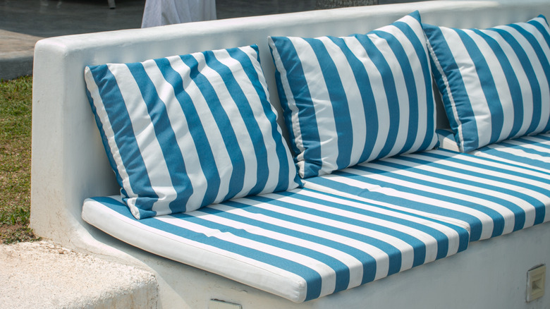 Striped white and blue outdoor cushion and three pillows outdoors on a bench