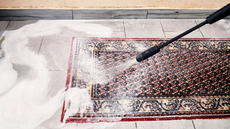 Pressure washer cleaning a rug, with soapy water running off the surface