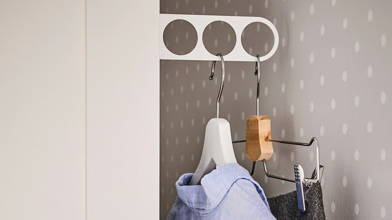 Two clothes hangers hang on a white KOMPLEMENT valet hanger inside a cabinet lined with gray polka dot paper