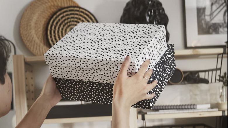 A person places two polka dot RÄTTAREN boxes on a wooden shelf