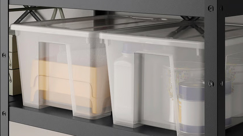 Two clear plastic storage boxes with lids sit on a black metal shelf in a garage