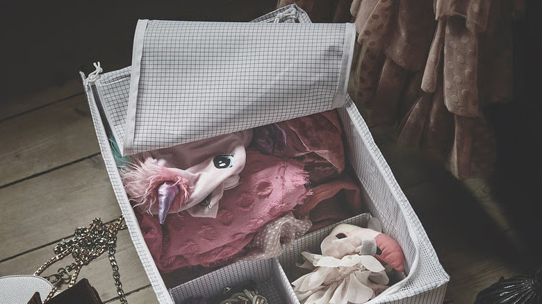 A large fabric IKEA storage box sitting on a wooden floor is unzipped to reveal pink clothes and accessories