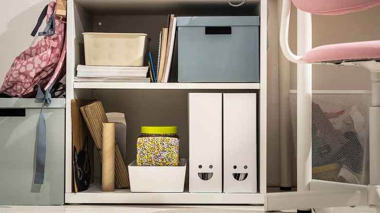 Two white upright IKEA TJABBA magazine files with smiley face cutouts sit on a shelf surrounded by office supplies