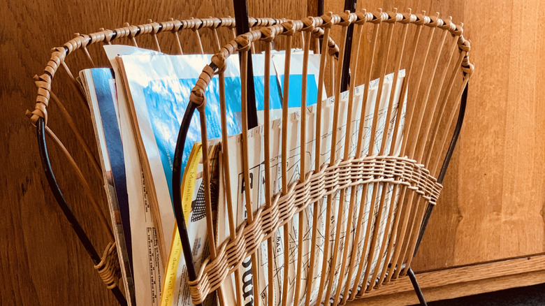 A metal and wicker magazine rack holding magazines.