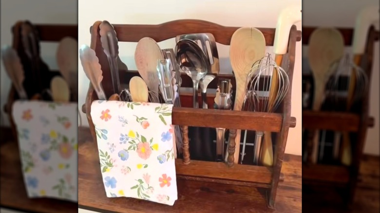 Cooking utensils and floral towel tucked into wooden rack