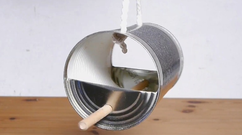 Cut tin can with wood perch for birds over wood surface