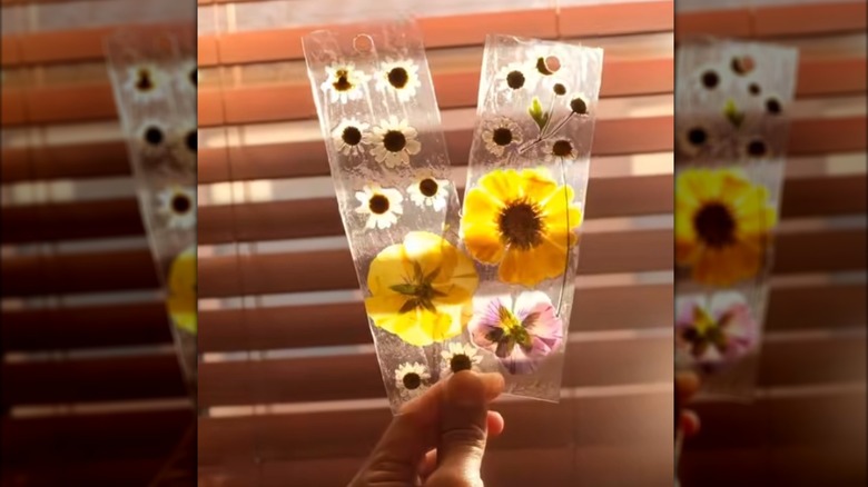 Woman holding DIY plastic bookmarks with flowers up to brightly lit window blinds