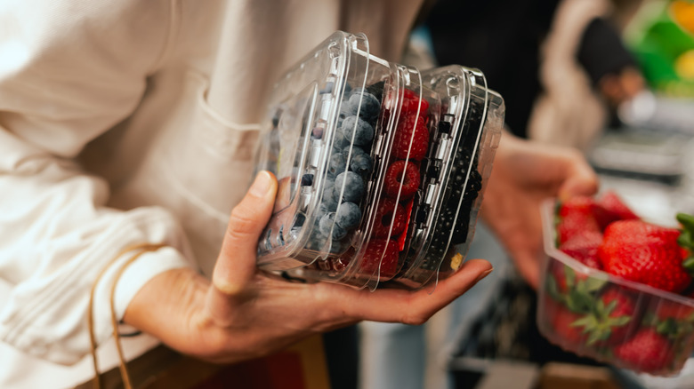 Woman holding multiple plastic fruit containers with various berries at store