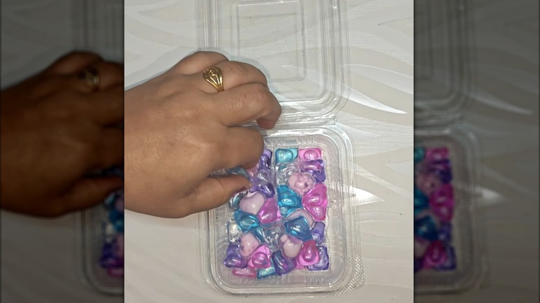 Colorful laundry pods in clear plastic square container on white surface