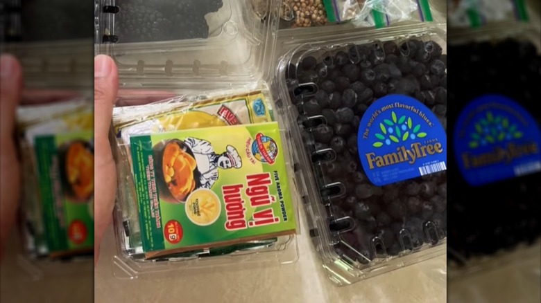 Woman tucking pre-packaged ingredients into empty blueberry container beside other packaged ingredients