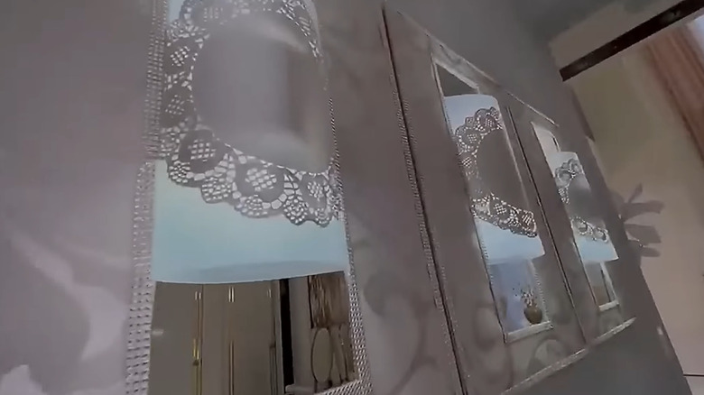 Tall wall-mounted mirrors with curved plastic decorated with doilies in the center.