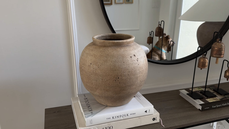 A textured brown vase sits on a stack of books displayed on an entryway table