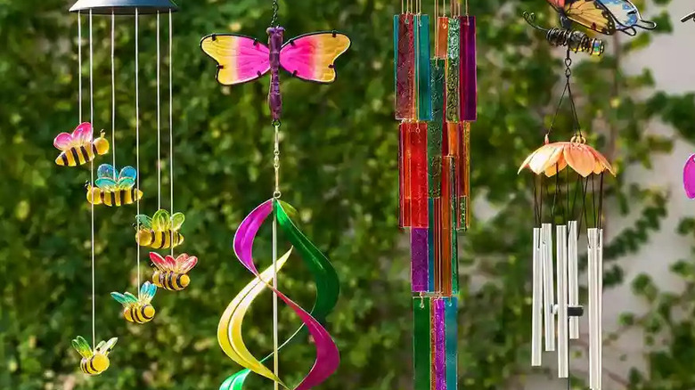 A collection of colorful windchimes hang next to each other in front of a vine-covered wall