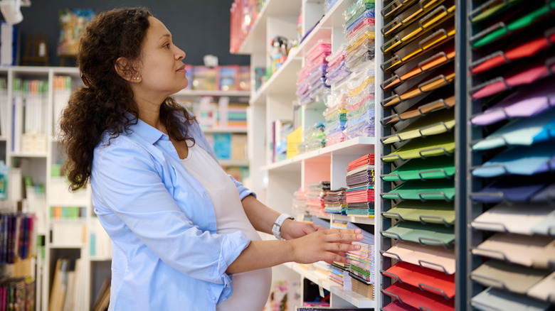 A pregnant woman shops for art supplies in a colorful craft store aisle