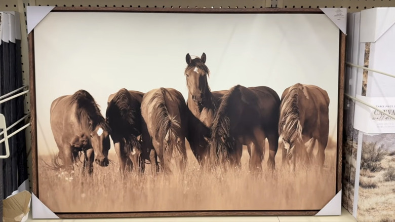 A framed print in a Hobby Lobby wall art display features a group of brown wild horses