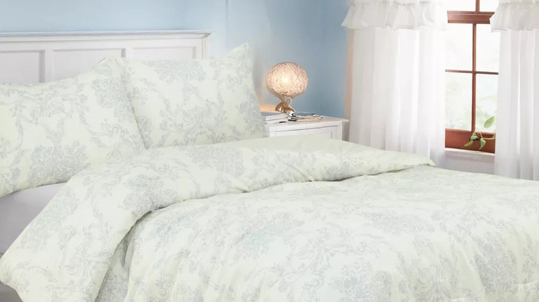 A light blue floral comforter set is on a bed in front of a window