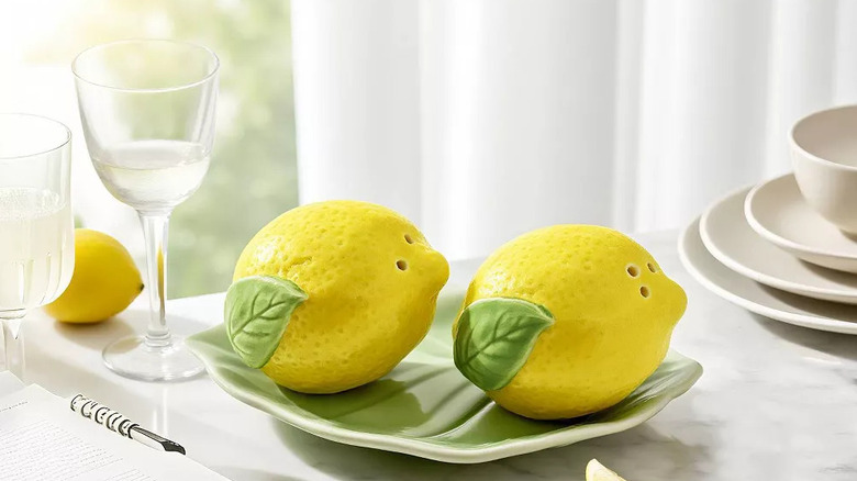A salt and pepper shaker set shaped like lemons sits on a matching tray on a marble countertop