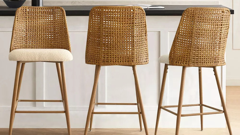 Three rattan-backed bar stools sit in front of a white counter with black countertop