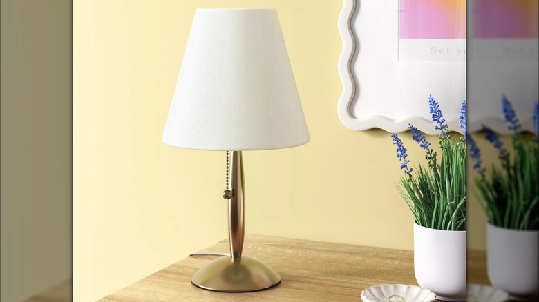 A small brass stick lamp sits on a wooden table next to a potted plant