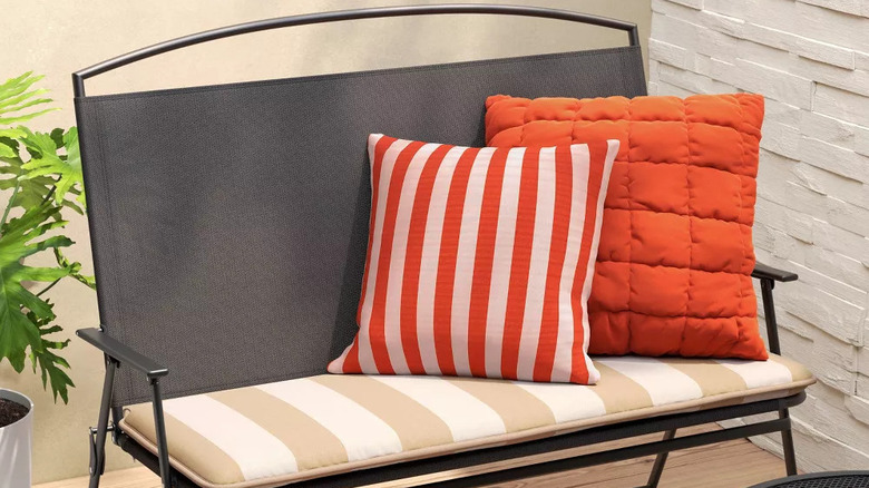 A bright striped cabana pillow sits on a simple black patio bench