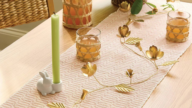 A gold metal botanical garland is woven between candles and glasses on a minimalist spring tablescape