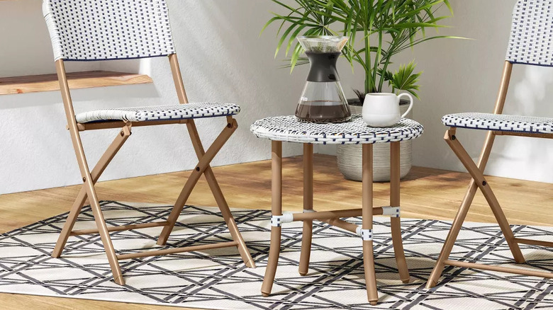 A carafe of coffee and mug sit on a small round cafe table between two matching patio chairs