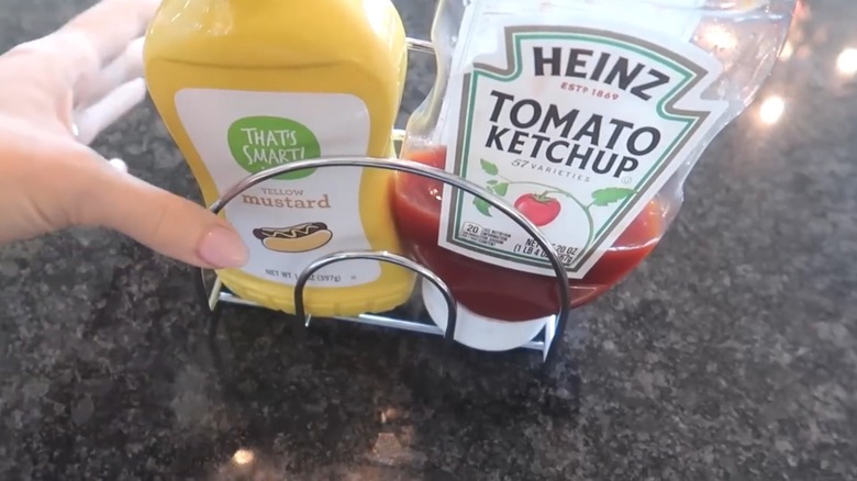 Yellow mustard and ketchup in wire napkin holder on stone-like countertop