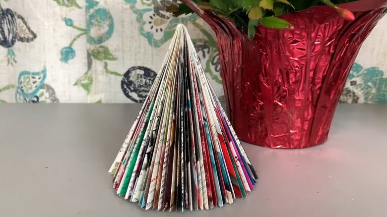 Magazine pages folded into decorative tree on white table besides Christmas flowers