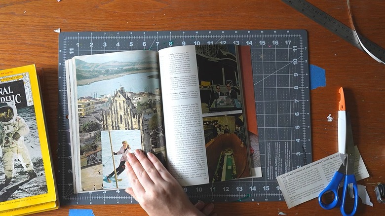 Person crafting with magazines over cutting mat with scissors and paper scraps
