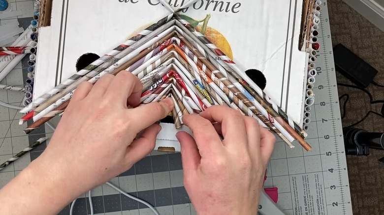 Woman gluing paper tubes to top of cardboard citrus box on cutting mat