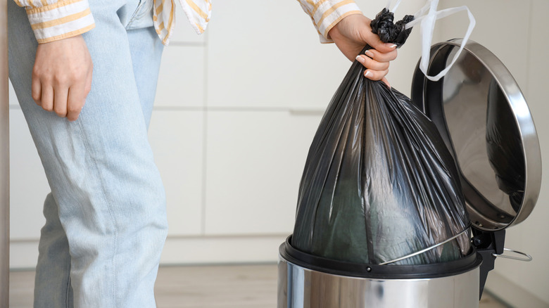 Woman removing trash bag from kitchen bin.