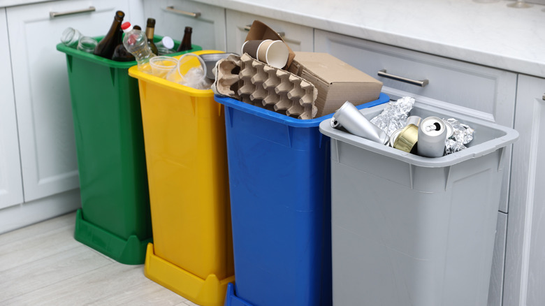 Four overflowing recycling bins in white kitchen.