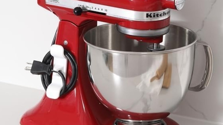 An Aieve Cord Organizer holding a cord on the side of a red Kitchenaid mixer