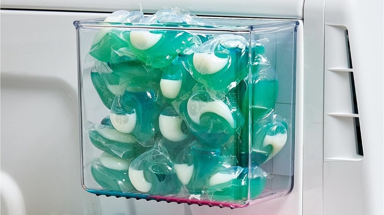 An iDesign Magnetic Plastic Organizer Bin on the side of a washing machine, holding detergent pods