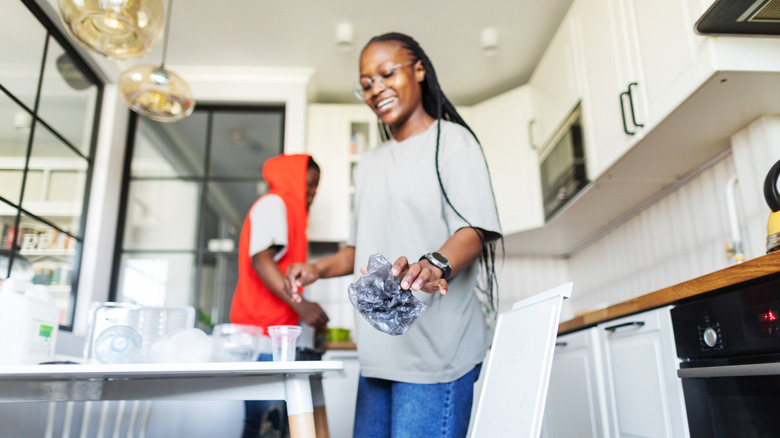 A woman holding a crumpled piece of plastic in a bright kitchen