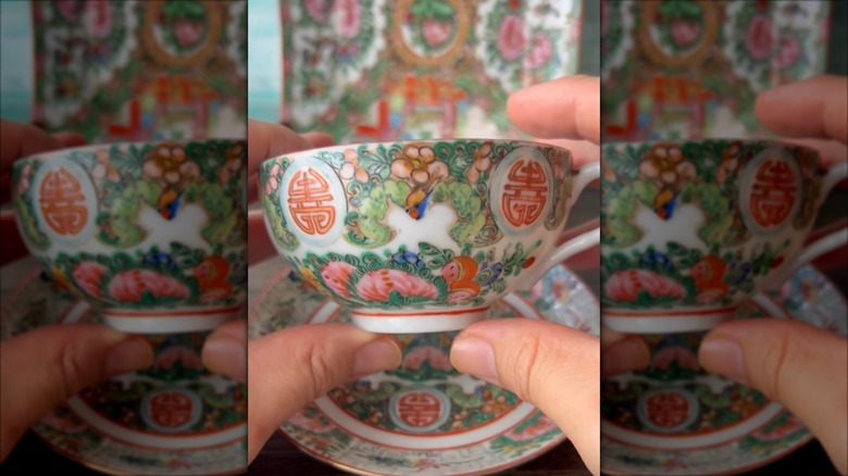A person holding a teacup featuring Chinese characters and flowers