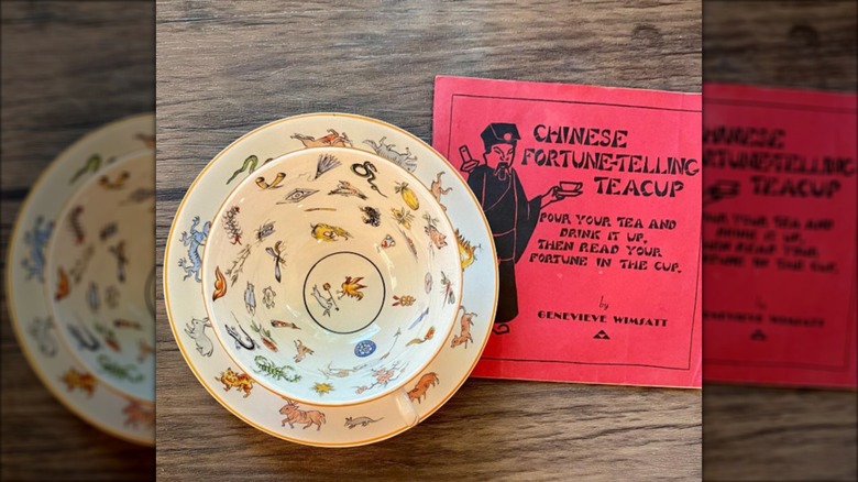 A teacup and saucer featuring images from Chinese mythology beside a red paper booklet
