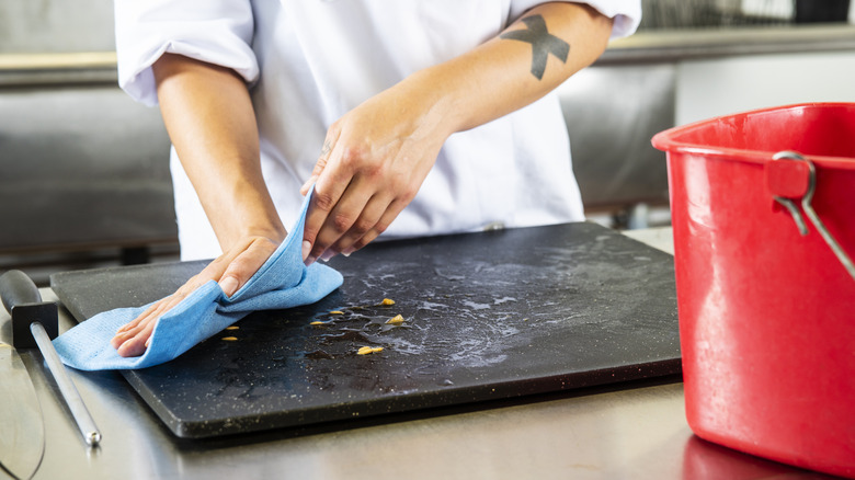a woman cleans off a cutting board with a blue rag