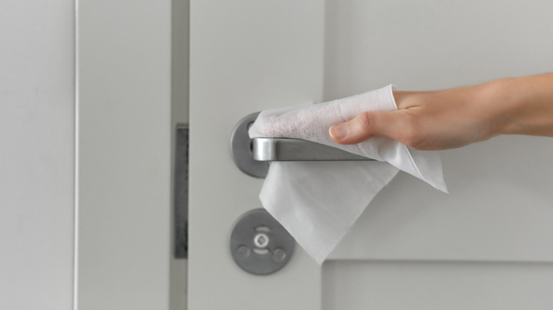 a person uses a wipe to clean a doorknob