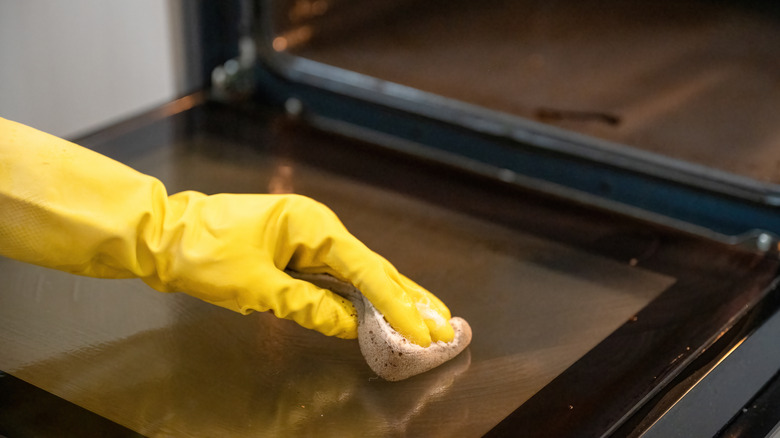 a person wearing a yellow glove cleans an oven door