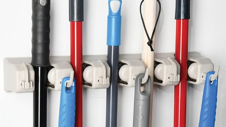 A mop and broom holder is laden with different kinds of cleaning tools