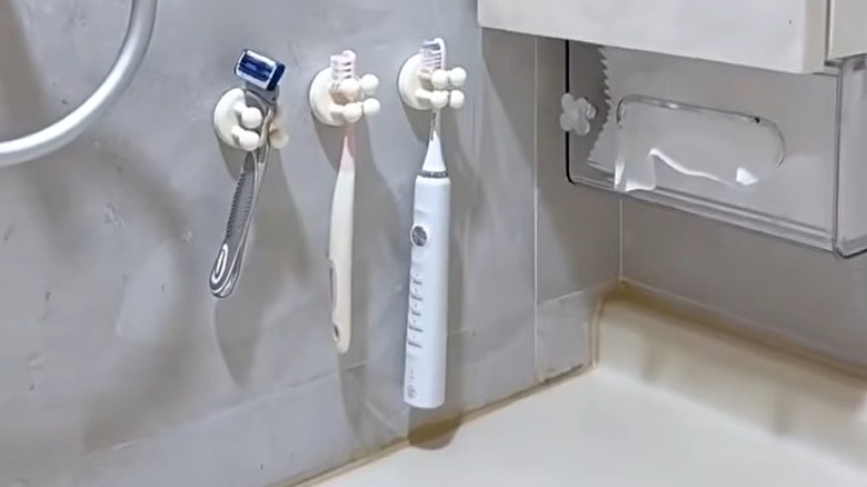 Silicone grippers holding a razor and two toothbrushes in a bathroom