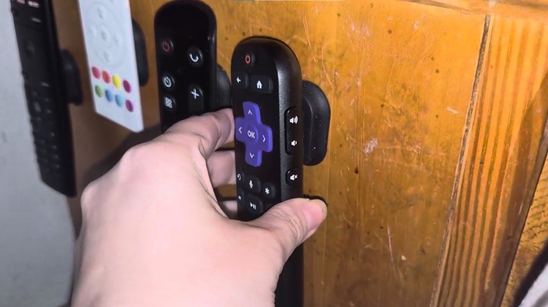 Four remotes hanging from a magnetic holder installed on wood cabinet